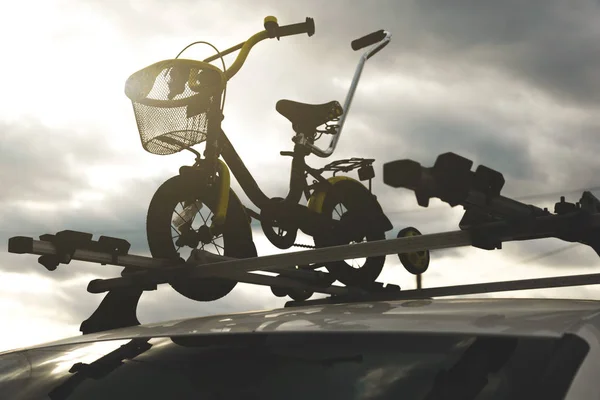 Bicycle transportation - a childrens bicycle on the roof of a car against the sky in a special mount for cycling. The decision to transport large loads and travel by car