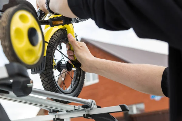 Transporte de bicicleta - Um homem prende e instala uma bicicleta infantil no telhado de um carro em uma montagem especial para transporte de bicicletas. A decisão de transportar grandes cargas e viajar de carro . — Fotografia de Stock