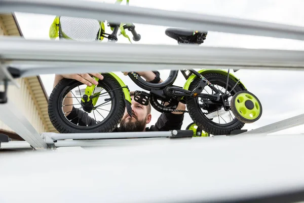 Bicycle transportation - A man fastens and installs a childrens bicycle on the roof of a car in a special mount for bicycle transport. The decision to transport large loads and travel by car.