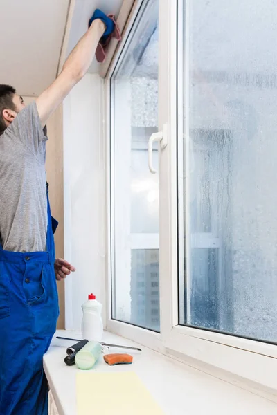 El primer plano de un hombre en uniforme y guantes azules lava las ventanas con rascador de ventanas. Servicio profesional de limpieza en el hogar — Foto de Stock