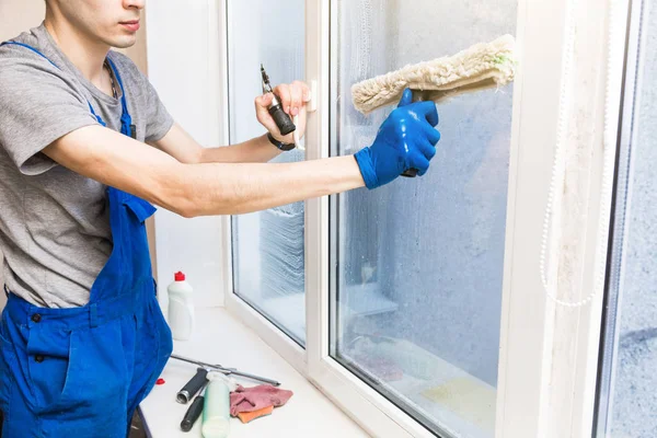 El primer plano de un hombre en uniforme y guantes azules lava las ventanas con rascador de ventanas. Servicio profesional de limpieza en el hogar — Foto de Stock
