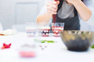 Bir şekerleştirici üç bardak içinde bir saçma hazırlar. Mutfaktaki beyaz masada tatlılar vardır. Ev yapımı pasta kavramı, yemek pastaları.