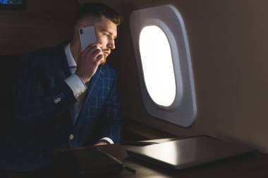 Genç, çekici ve başarılı bir iş adamı özel iş uçağında otururken telefonda konuşuyor ve çalışıyor.