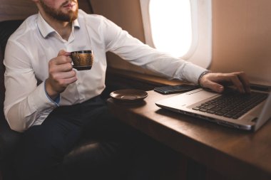 Çekici ve başarılı işadamı kahve içme ve onun özel jet bir sandalyede otururken bir laptop arkasında çalışma.