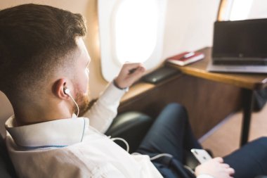 Genç ve başarılı iş adamı dinleniyor ve özel iş uçağının koltuğunda oturmuş müzik dinliyor.