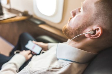 Genç ve başarılı iş adamı dinleniyor ve özel iş uçağının koltuğunda oturmuş müzik dinliyor.