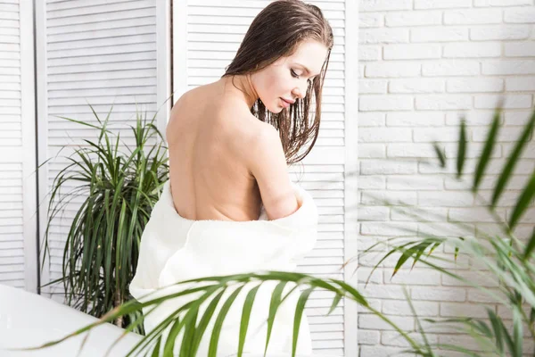 Attractive young girl in a white bathrobe applies cream to the skin while sitting in the interior of the bathroom and doing morning procedures. Skin and body care — Stock Photo, Image