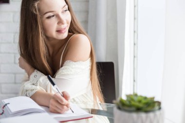 Bir gece elbisesi içinde güzel bir genç kız sabah bir cam masada oturuyor ve bir defter içinde düşüncelerini yazar.