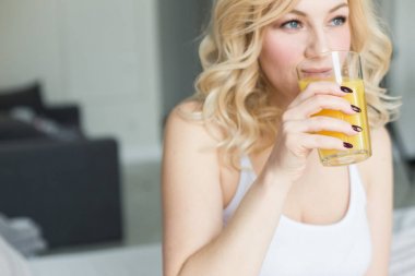 Çekici sarışın kadın evde yatağın kenarına oturmuş elinde portakal suyu olan bir çorap tutuyor. Sabah havası ve canlılık