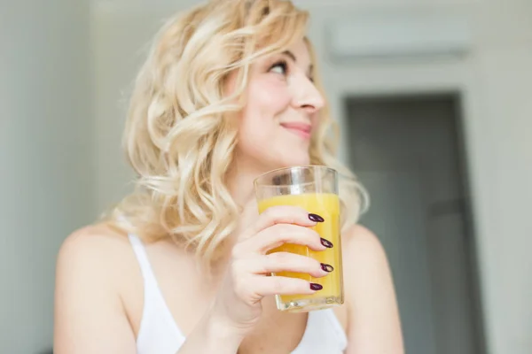 Aantrekkelijke blonde vrouw zit aan de rand van het bed thuis en houdt een kous met sinaasappelsap in haar hand. Ochtendstemming en kracht — Stockfoto