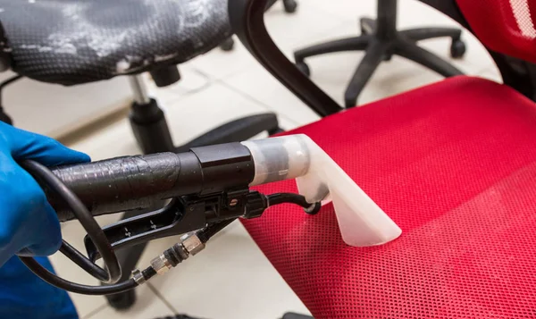 Ung man i arbetskläder och gummihandskar rengör kontorsstolen med professionell utrustning. — Stockfoto