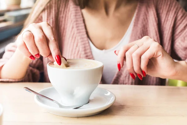 Ein Mädchen wirft ein Stück Zucker in den Kaffee. Nahaufnahme der Hände mit roten Nägeln Make-up und Cappuccino-Tasse — Stockfoto