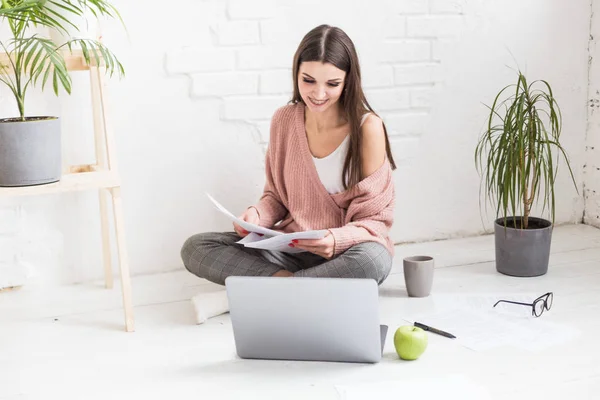 Mujer joven se sienta en el suelo en un interior de apartamento escandinavo con una computadora portátil, estudiar derecho, chica independiente en el trabajo, estudiante de educación a distancia, empleo en línea, papeleo y concepto de externalización — Foto de Stock