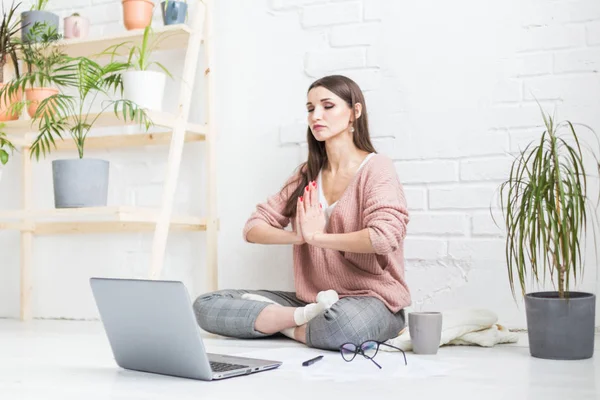 Молода щаслива жінка сидить на підлозі в позі йоги в світлій квартирі і працює за ноутбуком, дівчина-фрілансер медитує під час роботи. зняття стресу — стокове фото