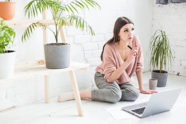 Mujer joven se sienta en el suelo en un interior de apartamento escandinavo con una computadora portátil, estudiar derecho, chica independiente en el trabajo, estudiante de educación a distancia, empleo en línea, papeleo y concepto de externalización — Foto de Stock