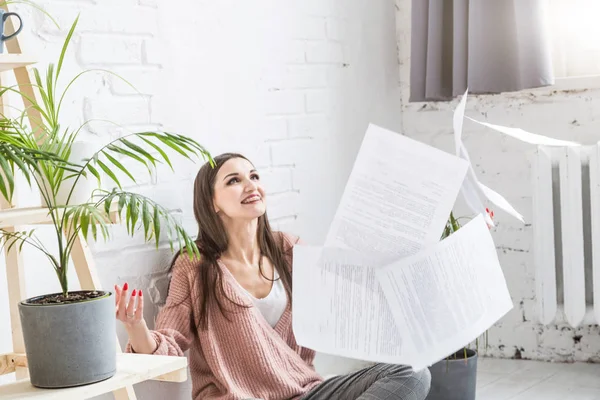 Una joven mujer feliz vomita un montón de papeles y documentos sentados cerca del portátil, la chica independiente está feliz y de buen humor. emoción e inspiración — Foto de Stock