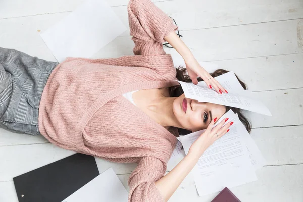 Красива жінка лежить на підлозі серед паперів і документів, дівчина фрілансер посміхається і відпочиває під час перерви від роботи — стокове фото