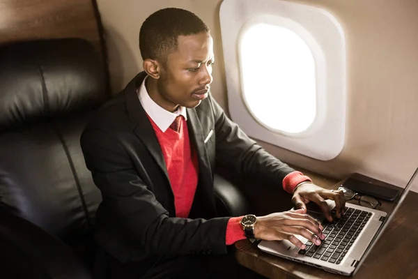 Attractive and successful African American businessman with glasses working on a laptop while sitting in the chair of his private jet
