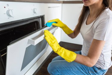 Profesyonel temizlik şirketinden genç bir kadın evi temizliyor. Bir adam mutfağı temizlik malzemeleriyle sarı eldivenlerle yıkıyor..