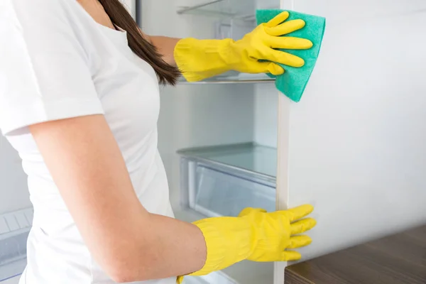 A young woman from a professional cleaning company cleans up at home. A man washes the kitchen washes the fridge in yellow gloves with cleaning supplies stuff. — Stock Photo, Image