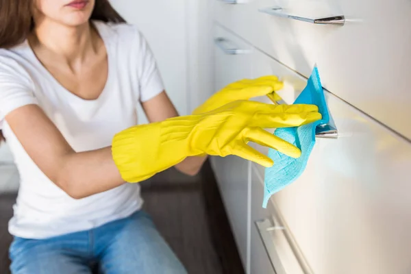 Profesyonel temizlik şirketinden genç bir kadın evi temizliyor. Bir adam mutfağı temizlik malzemeleriyle sarı eldivenlerle yıkıyor.. — Stok fotoğraf