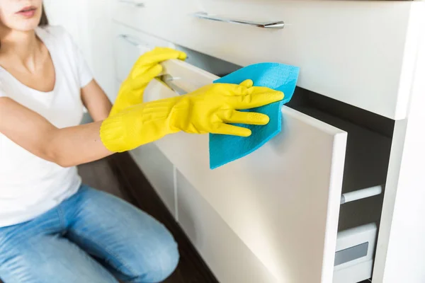 Μια νεαρή γυναίκα από μια επαγγελματική εταιρεία καθαρισμού καθαρίζει στο σπίτι. Ένας άντρας πλένει την κουζίνα με κίτρινα γάντια με καθαριστικά.. — Φωτογραφία Αρχείου