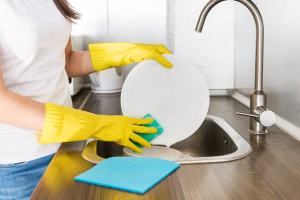 Una joven con guantes amarillos lava platos con una esponja en el fregadero. Servicio de limpieza profesional de casas . —  Fotos de Stock