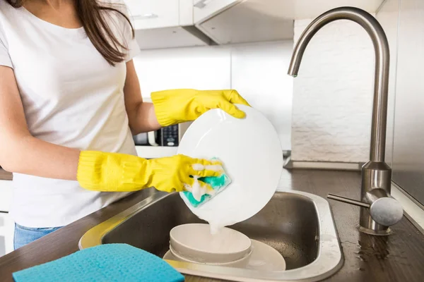 Una joven con guantes amarillos lava platos con una esponja en el fregadero. Servicio de limpieza profesional de casas . —  Fotos de Stock