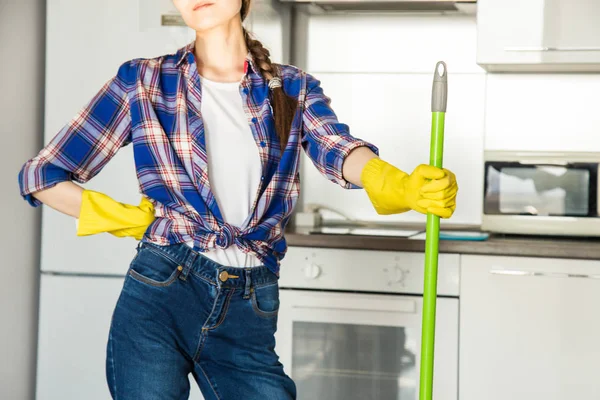 En ung kvinna städar hemma, tvättar köket. Skopa med trasor och gula handskar på bordet — Stockfoto