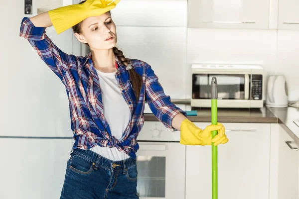 Молодая женщина убирает дома, моет кухню. Ведро с тряпками и желтыми перчатками на столе — стоковое фото