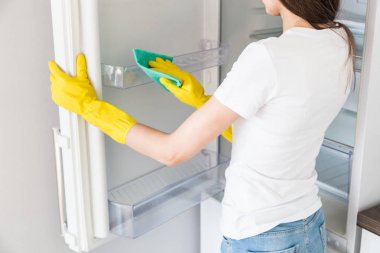 Profesyonel temizlik şirketinden genç bir kadın evi temizliyor. Bir adam mutfağı yıkıyor ve buzdolabını sarı eldivenlerle temizliyor..
