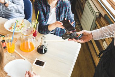Genç ve çekici bir kadın, kafeteryada bağlantısız akıllı telefon ödemesiyle ödeme yapıyor.