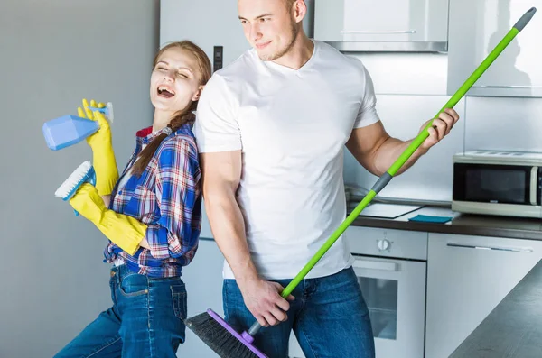 Pareja joven marido y mujer limpian la casa. El chico y la chica lavan la cocina con una fregona y un paño, trabajo en equipo, diversión —  Fotos de Stock