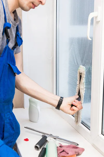 El primer plano de un hombre en uniforme y guantes azules lava las ventanas con rascador de ventanas. Servicio profesional de limpieza en el hogar — Foto de Stock