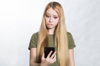 Şaşırtılmış ve endişeli genç bir kadın bir akıllı telefon tutarak, sürpriz bir ifade ile bakıyor.