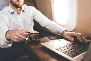 Çekici ve başarılı işadamı kahve içme ve onun özel jet bir sandalyede otururken bir laptop arkasında çalışma.