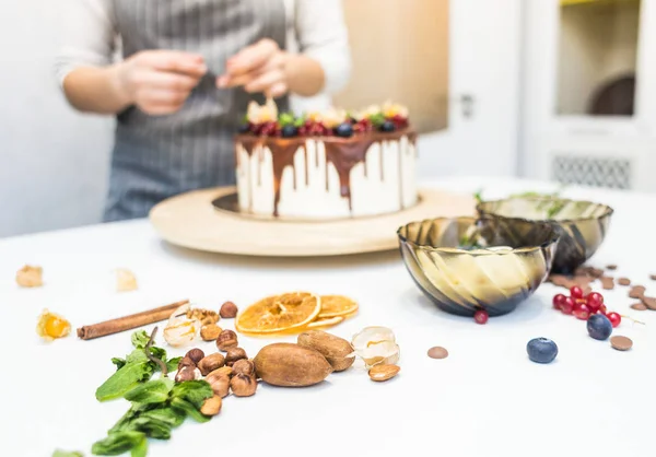 Cukrászda díszíti bogyókat keksz torta, fehér tejszín és csokoládé. A sütemény egy fából készült állványon áll egy fehér asztalon. A koncepció a házi készítésű péksütemények, főzősütemények. — Stock Fotó