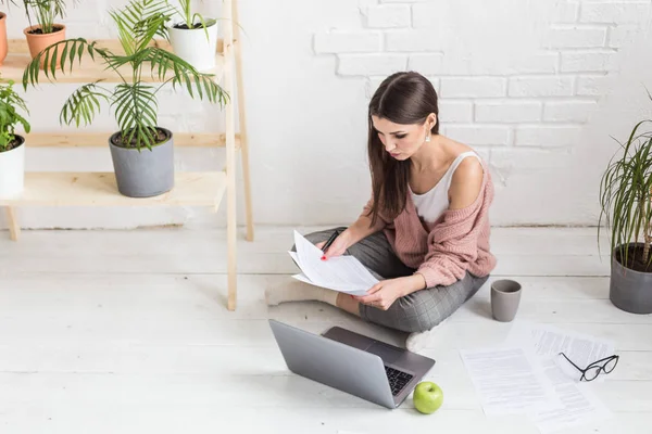 Μια νεαρή ευτυχισμένη γυναίκα κάθεται στο πάτωμα σε ένα φωτεινό διαμέρισμα ή εσωτερικό γραφείο και εργάζεται σε ένα φορητό υπολογιστή, ελεύθερος επαγγελματίας κορίτσι στην εργασία, η έννοια της εξ αποστάσεως μάθησης φοιτητές, γραφειοκρατία και online μάθηση — Φωτογραφία Αρχείου