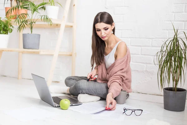 Jonge vrouw zit op de vloer in een Scandinavisch appartement interieur met een laptop, studeren rechten, freelance meisje op het werk, afstandsonderwijs student, online werkgelegenheid, papierwerk en outsourcing concept — Stockfoto