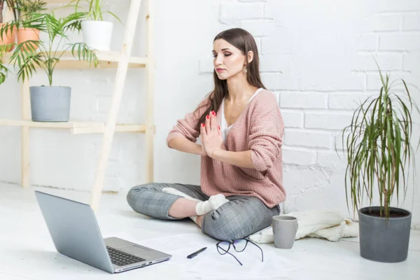 Молода щаслива жінка сидить на підлозі в позі йоги в світлій квартирі і працює за ноутбуком, дівчина-фрілансер медитує під час роботи. хвилювання та натхнення — стокове фото