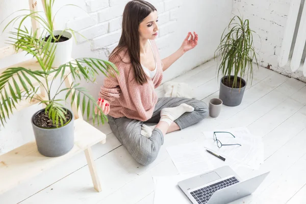 Jovem mulher feliz senta-se no chão em uma pose de ioga em um apartamento brilhante e trabalha atrás de um laptop, uma menina freelancer medita enquanto trabalha. Stress do trabalho — Fotografia de Stock