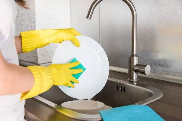 Una joven con guantes amarillos lava platos con una esponja en el fregadero. Servicio de limpieza profesional de casas . —  Fotos de Stock