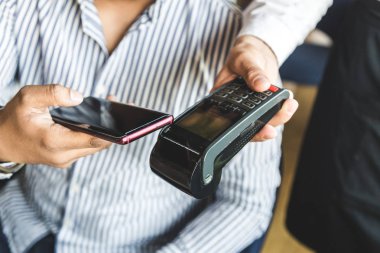 Genç, çekici Hindu adam, kafeteryada, bağlantısız akıllı telefon ödemesiyle ödeme yapıyor.