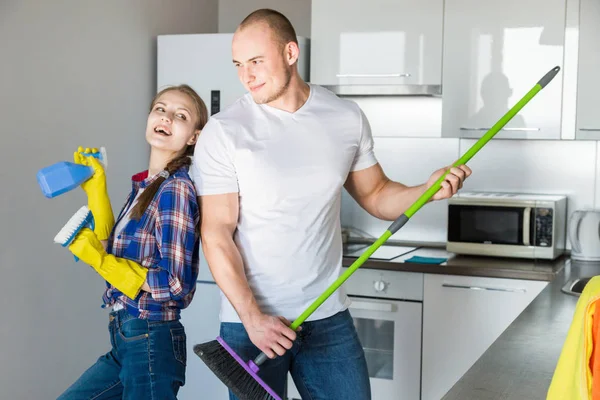 Молодые супруги занимаются уборкой дома. Парень и девушка моют кухню шваброй и тряпкой, командная работа, веселье — стоковое фото
