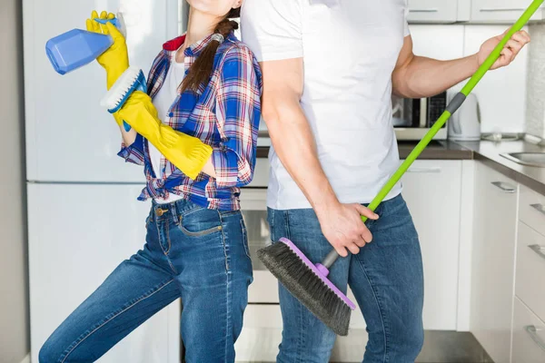 Молодые супруги занимаются уборкой дома. Парень и девушка моют кухню шваброй и тряпкой, командная работа, веселье — стоковое фото