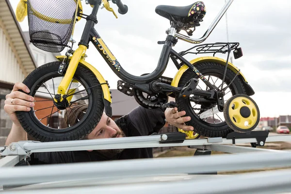 Transporte de bicicleta - Um homem prende e instala uma bicicleta infantil no telhado de um carro em uma montagem especial para transporte de bicicletas. A decisão de transportar grandes cargas e viajar de carro . — Fotografia de Stock