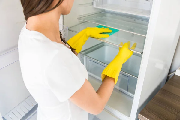 A young woman from a professional cleaning company cleans up at home. A man washes the kitchen washes the fridge in yellow gloves with cleaning supplies stuff. Stock Photo