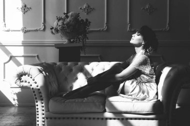 Bir ipek cüppe güzel genç seksi sarışın kadın olay ışık ışınları bir pencereönünde bacaklarını sarılma bir kanepede oturan