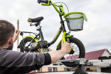 Bisiklet taşımacılığı - Bir adam bağlar ve bisiklet taşımacılığı için özel bir binek bir arabanın çatısına bir çocuk bisiklet yükler. Büyük yükleri taşıma ve araba ile seyahat kararı.