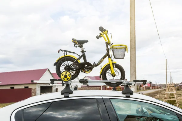 Fiets vervoer-een Kinderfiets op het dak van een auto tegen de hemel in een speciale berg om te fietsen. De beslissing om grote ladingen te vervoeren en te reizen met de auto — Stockfoto